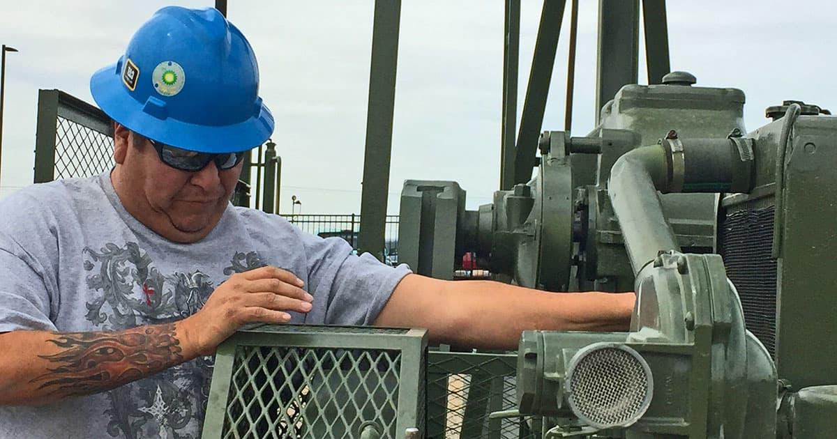 Man, wearing a blue hardhat, working on oil and gas equipment.